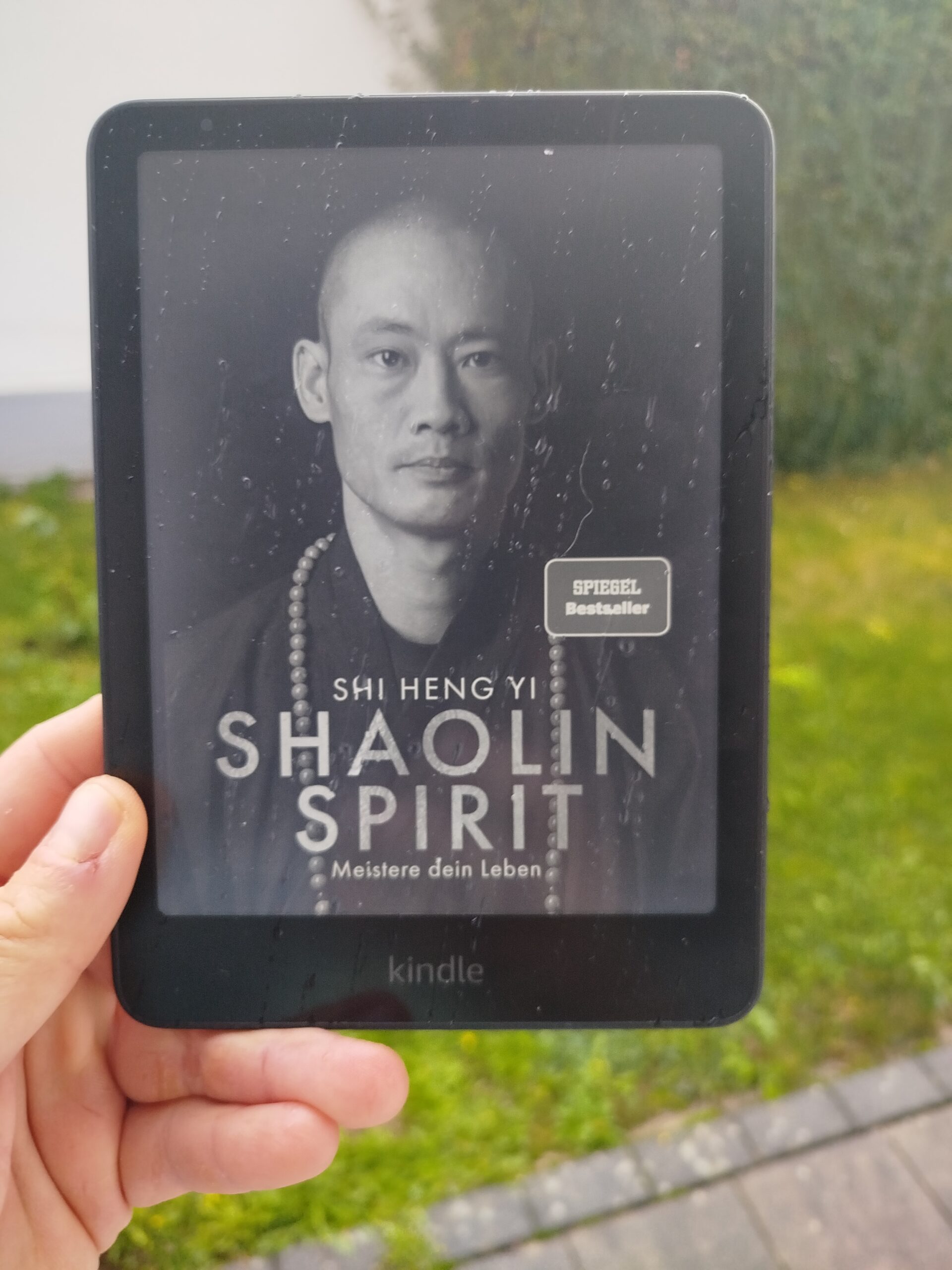 Das Buchcover von 'Shaolin Spirit' von Shi Heng Yi, angezeigt auf einem Kindle-Reader, der im Freien in einer Hand gehalten wird.
