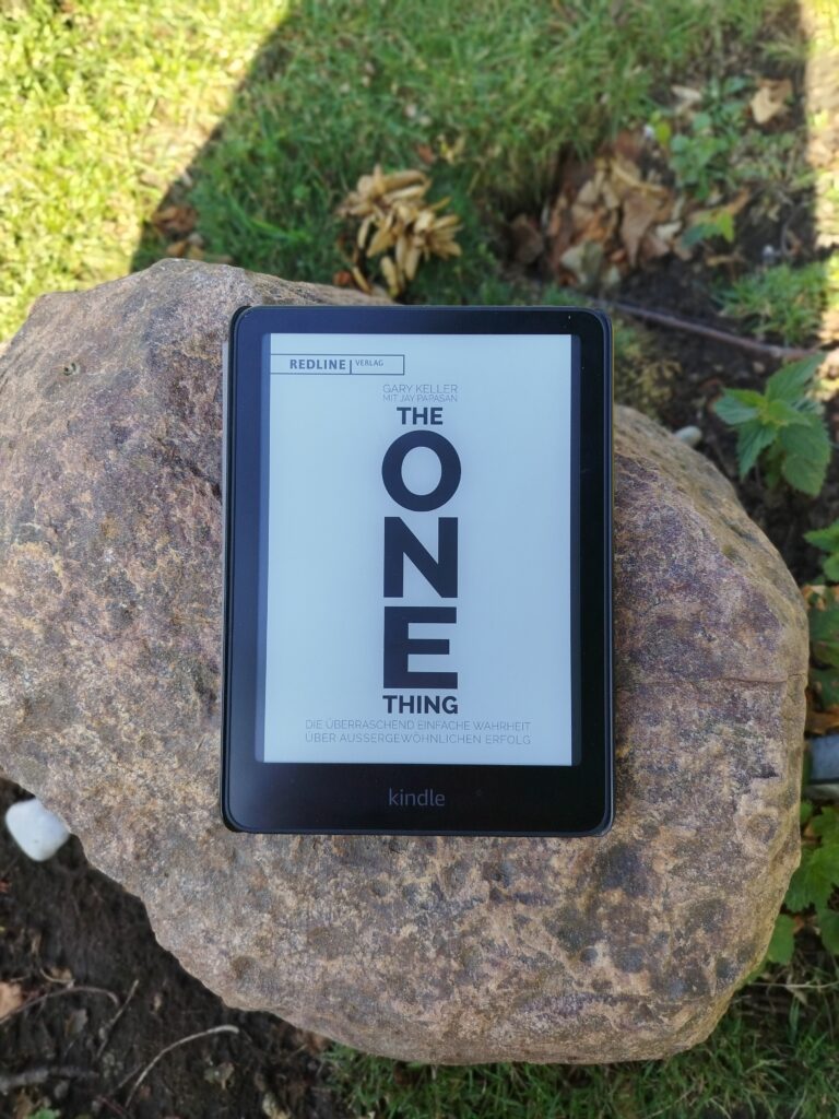 Das Buchcover von The ONE Thing von Gary Keller auf einem Kindle, der draußen auf einem großen Felsen liegt.