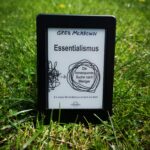 Ein Kindle E-Reader zeigt das Cover des Buches Essentialismus von Greg McKeown, das in einer grünen Wiese steht.