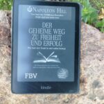 Das Buchcover von Der geheime Weg zu Freiheit und Erfolg von Napoleon Hill auf einem Kindle, der draußen auf einem Naturstein liegt.