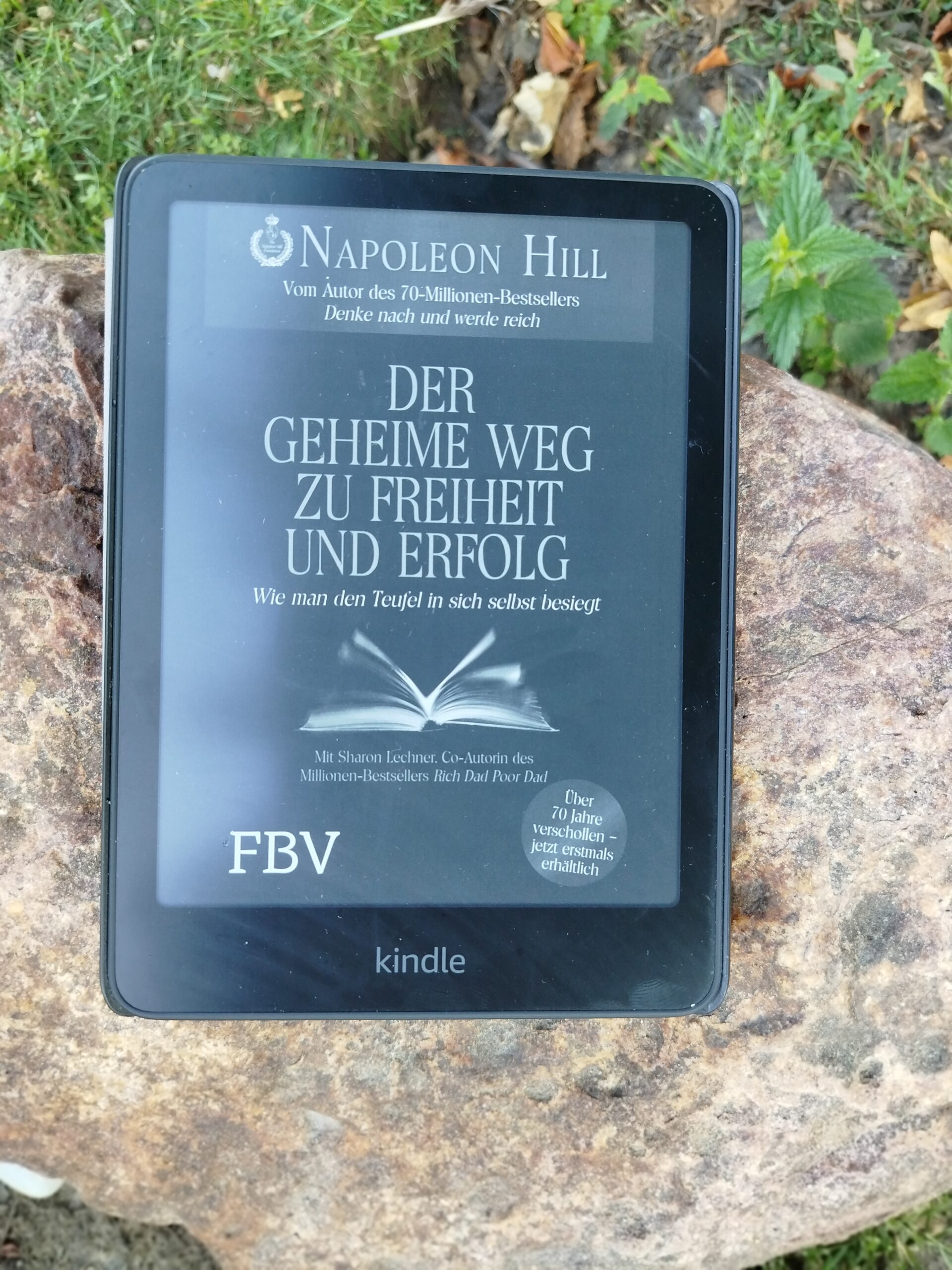 Das Buchcover von Der geheime Weg zu Freiheit und Erfolg von Napoleon Hill auf einem Kindle, der draußen auf einem Naturstein liegt.