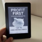 Das Buch Profit First in der Hand auf einem Kindle erkennbar